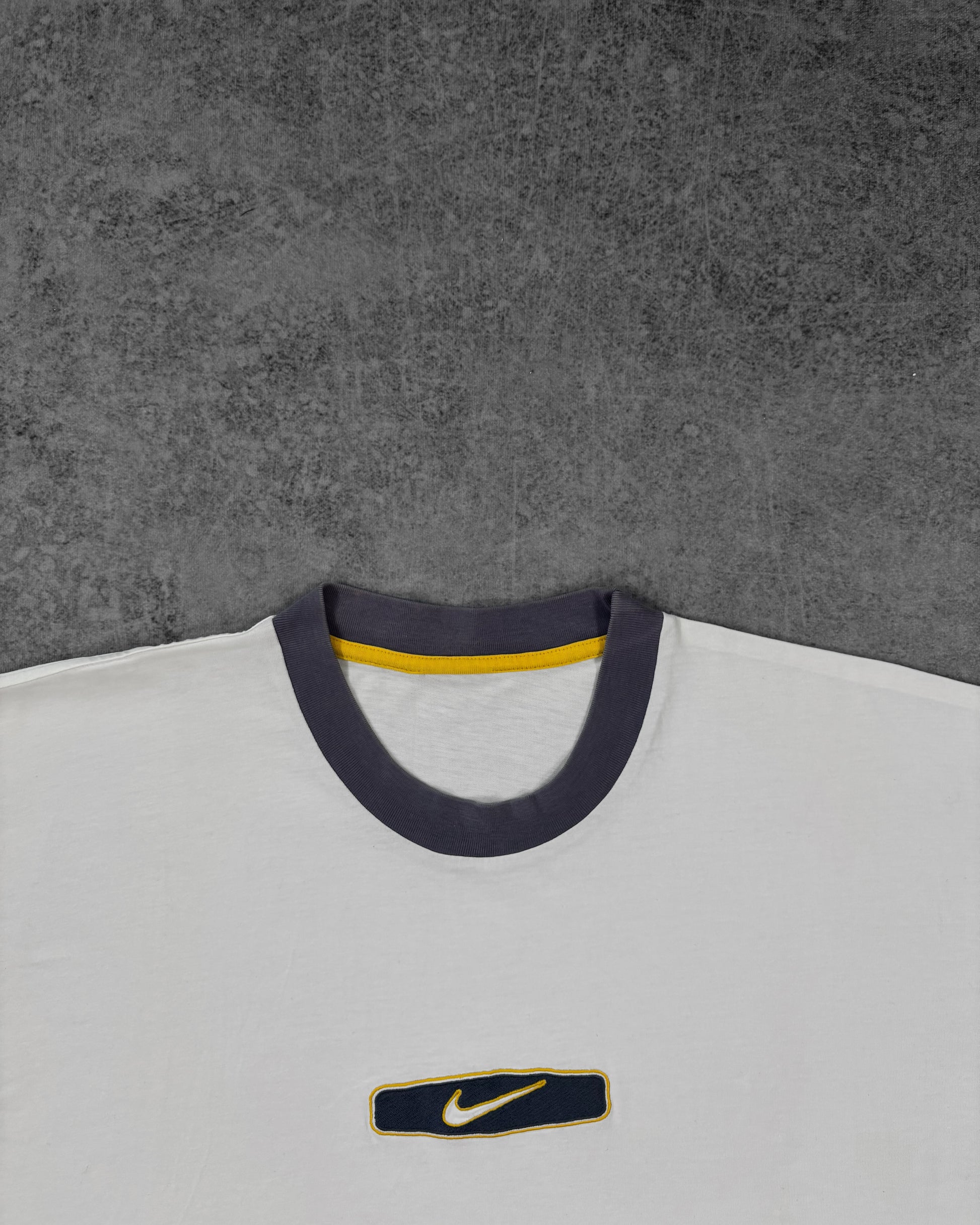 Detail of the embroidered Nike Swoosh patch on the chest in navy and yellow
